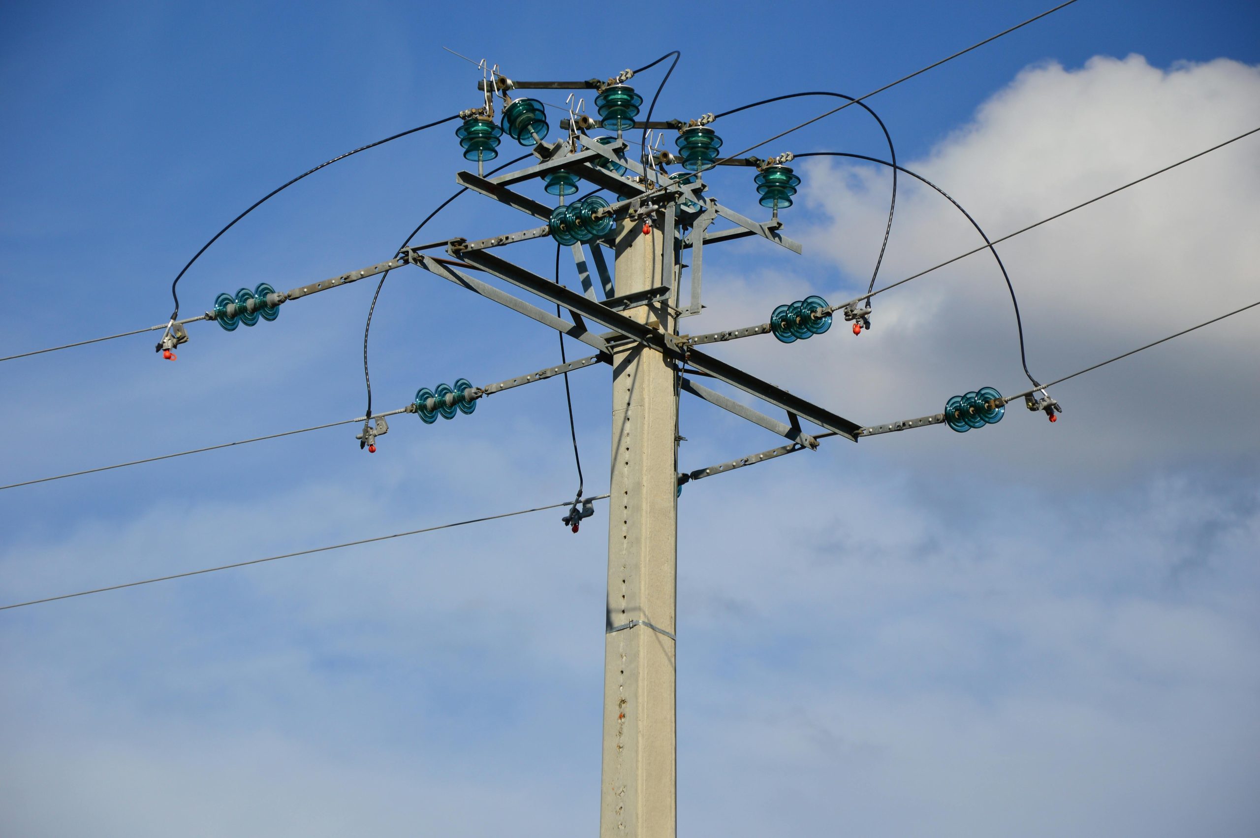 A high voltage power line stretching against a clear blue sky with clouds.